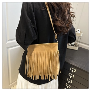 Detail of khaki suede shoulder bag with long fringes worn by a model in a minimal setting