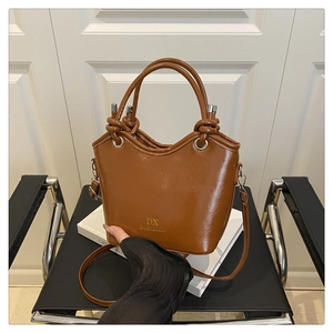 Detail of a brown leather bucket bag featuring a gold logo and stylish knotted handle