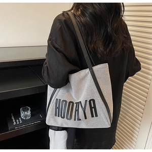 Detail of grey canvas tote bag with black shoulder straps and HOOAYA logo in urban setting