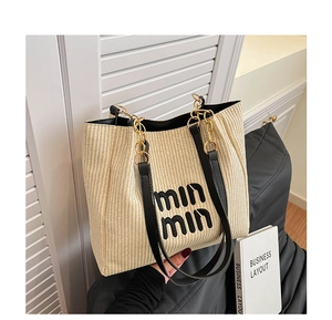 Detail of straw woven tote bag featuring black leather trim and gold chain handle straps