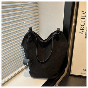Detail of a black matte leather tote bag with a thin knotted strap and circular leather charm
