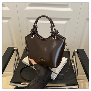 Detail of dark brown glossy patent leather bucket bag with golden brand logo and knotted handle