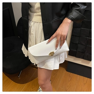 Detail of white envelope clutch featuring a gold leaf-shaped clasp and matte leather finish
