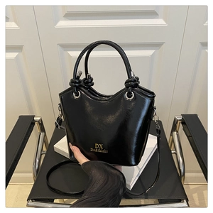 Detail of glossy black handbag with gold logo and decorative knotted handle on books