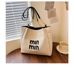 Detail of beige woven tote bag with black min min logo and chain leather straps