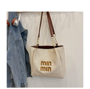 Detail of woven beige tote bag with brown leather straps and gold metal chain hardware