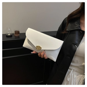 White envelope clutch featuring a gold leaf clasp held against a minimalist background