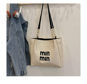 Detail of cream woven tote bag with chain strap and embroidered logo in lifestyle setting