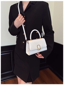 Detail of white crocodile embossed baguette bag with golden clasp and metal handle