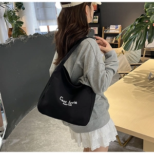 Détail du sac fourre-tout en toile noire avec lettrage blanc porté par un mannequin