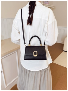 Detail of black crocodile texture baguette bag with golden metal buckle on white shirt