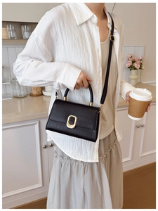 Close-up of black crocodile-embossed leather bag with a gold oval clasp and top handle