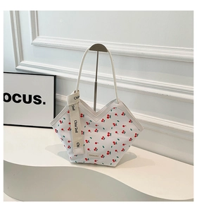 Close-up of white tote bag with red cherry prints and decorative branded strap detail