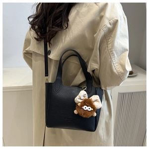Detail of black pebbled leather bucket bag featuring a cute plush monster charm on the strap