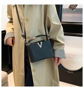 Detail of black wave pattern leather handbag with gold V-clasp on beige trench coat