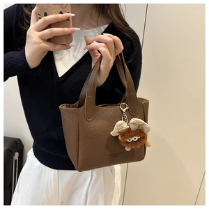 Détail du sac seau marron à motif litchi avec doubles poignées et pendentif monstre