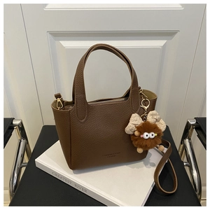 Détail d'un sac seau marron en cuir grainé avec charm en peluche sur des livres