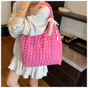Pink pleated tote bag with white lace bow detail shown on shoulder in a cozy home setting