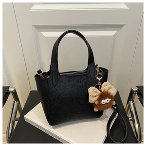 Détail d'un sac seau en cuir grainé noir avec charme monstre peluche sur un livre