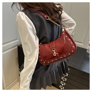 Macro shot of bright red patent leather hobo bag with gold studs and metal hook detail
