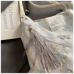 Detailed embroidery of blue butterflies and gray tassel on a beige fabric tote bag