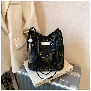 Detail of black tote bag featuring golden butterfly prints and a gray tassel accessory