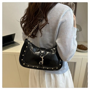 Detail of black leather crescent bag with gold studs and chain strap in a lifestyle setting
