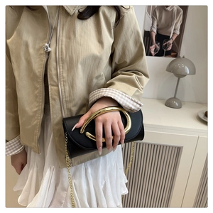 Detail of black leather clutch with oversized gold metal ring handle and chain strap