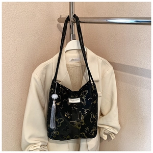 Detail of black tote bag with gold butterfly prints and a decorative grey tassel pendant