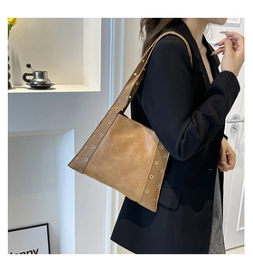 Sac sous le bras en cuir marron avec œillets métalliques porté par un mannequin en costume