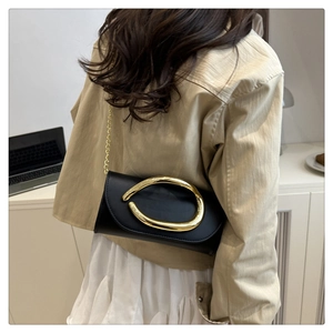 Detail of black leather clutch with unique gold metal buckle and elegant chain strap
