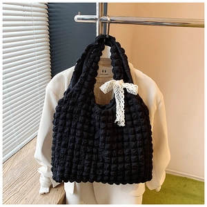 Detail of black popcorn texture tote bag featuring a white lace bow charm and soft fabric