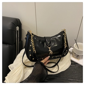 Detail of a black patent leather crescent bag with gold studs on a soft white silk fabric