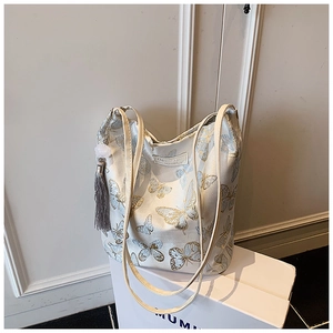 Detail of floral butterfly embroidery on off-white canvas tote bag with silk tassel accent