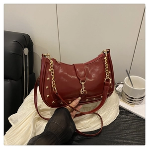 Detail of burgundy crescent bag with glossy patent leather and gold stud accents
