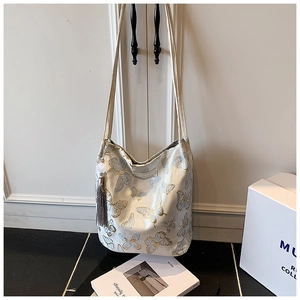 Detail of white canvas tote bag featuring intricate blue and gold butterfly embroidery and tassel