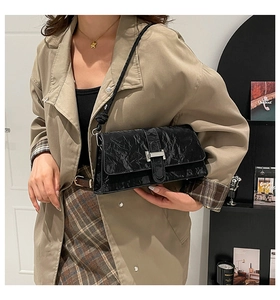 Détail d'un sac à bandoulière en cuir froissé noir avec boucle argentée sur un manteau