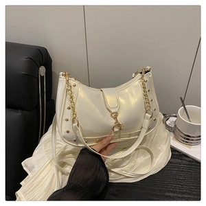 Detail of pearlescent white underarm bag with gold rivets and chain strap on leather seat
