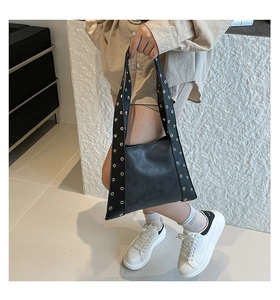 Détail d'un sac cabas en cuir noir avec œillets métalliques dorés et large bandoulière