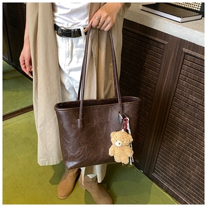 Detail of dark brown faux leather tote bag featuring fashion metal logo and teddy bear charm