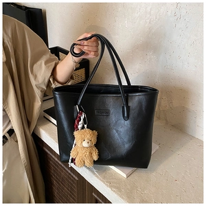 Detail of matte black tote bag with lychee texture, fashion logo and bear charm
