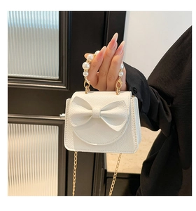 Detail of white mini bag with pearl handle, bow decoration and gold chain strap