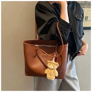 Close-up of brown PU leather tote bag featuring a Fashion label and plush bear charm