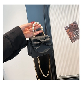 Macro detail of black litchi grain mini bag with oversized bow and pearl handle chain