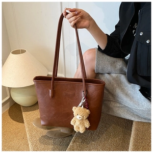 Close-up of brown PU leather tote bag with FASHION embossing and a cute plush bear charm