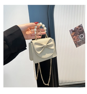 Detail of beige bow mini bag with pearl handle, litchi texture and gold chain strap