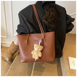 Detailed back view of a brown tote bag with bear charm and silk scarf on a model
