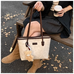 Fashionable beige tote bag with brown handles and a cute teddy bear charm on a street