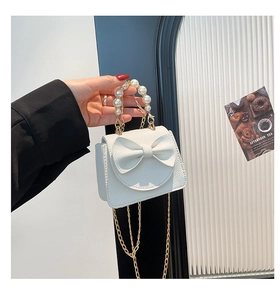 Detail of white mini bow bag with pearl handle and golden chain strap held by hand