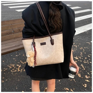 Detail of beige tote bag with dark brown trim, plush bear charm and autumn street background